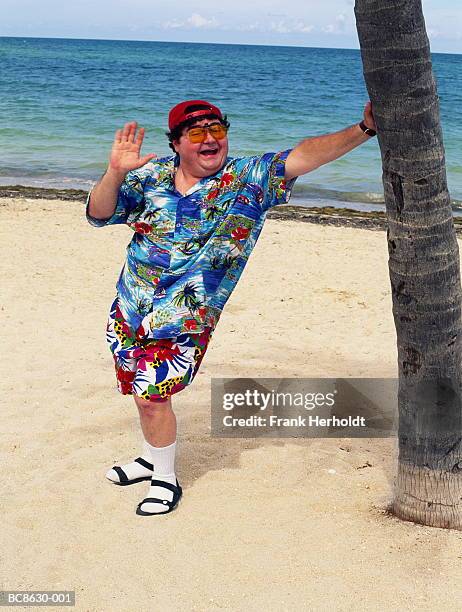 overweight-man-standing-on-beach-leaning-on-palm-tree-waving.jpg
